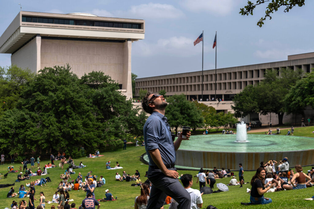 One man looks up at wearing eclipse glasses near a large crowd of students, faculty and staff gathered near the LBJ fountain on UT campus.