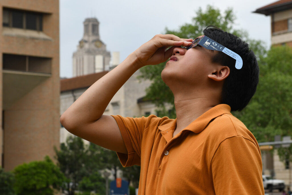 Student on campus looking up at the eclipse through longhorn eclipse glasses.