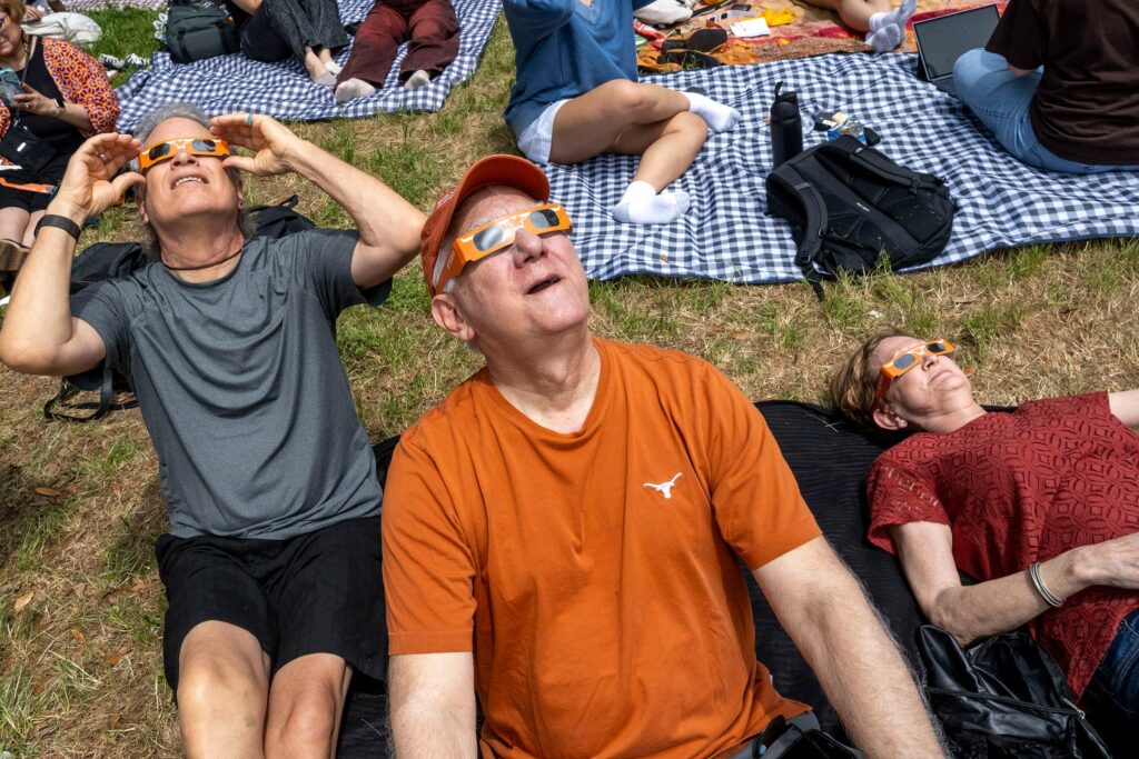 Alumni on blankets on campus looking up at the eclipse through longhorn eclipse glasses.
