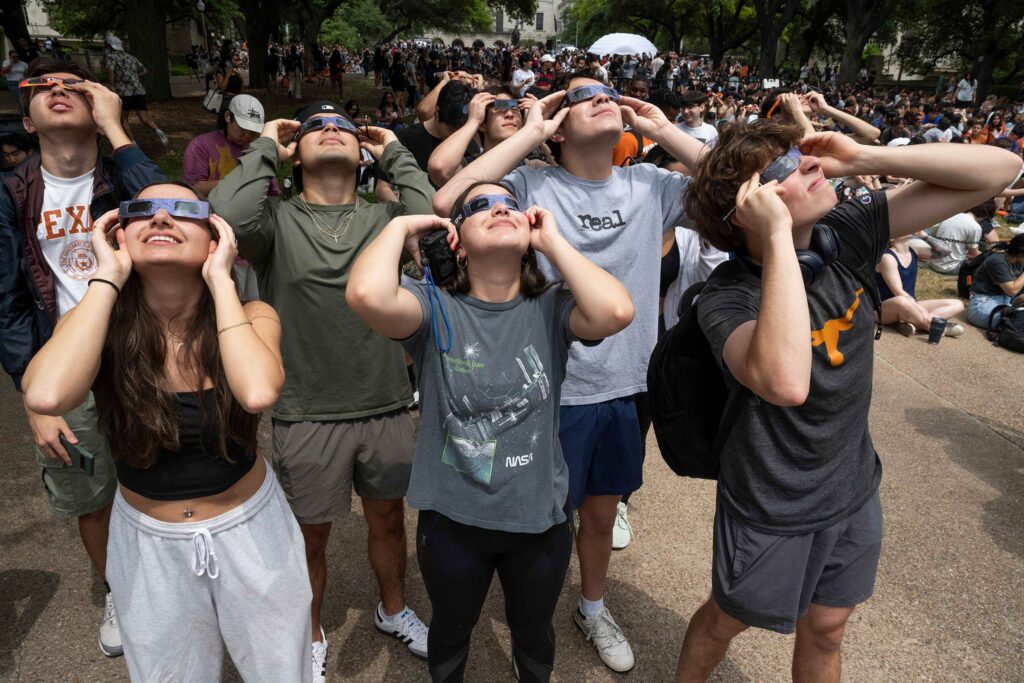Large crowd of students, faculty and staff on campus looking up at the eclipse through longhorn eclipse glasses.