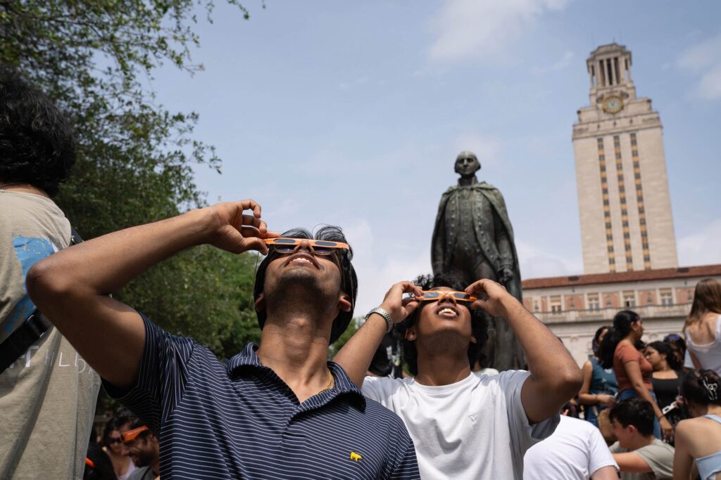 Students, Faculty and staff on campus looking up at the eclipse through longhorn eclipse glasses in front of the UT Tower.