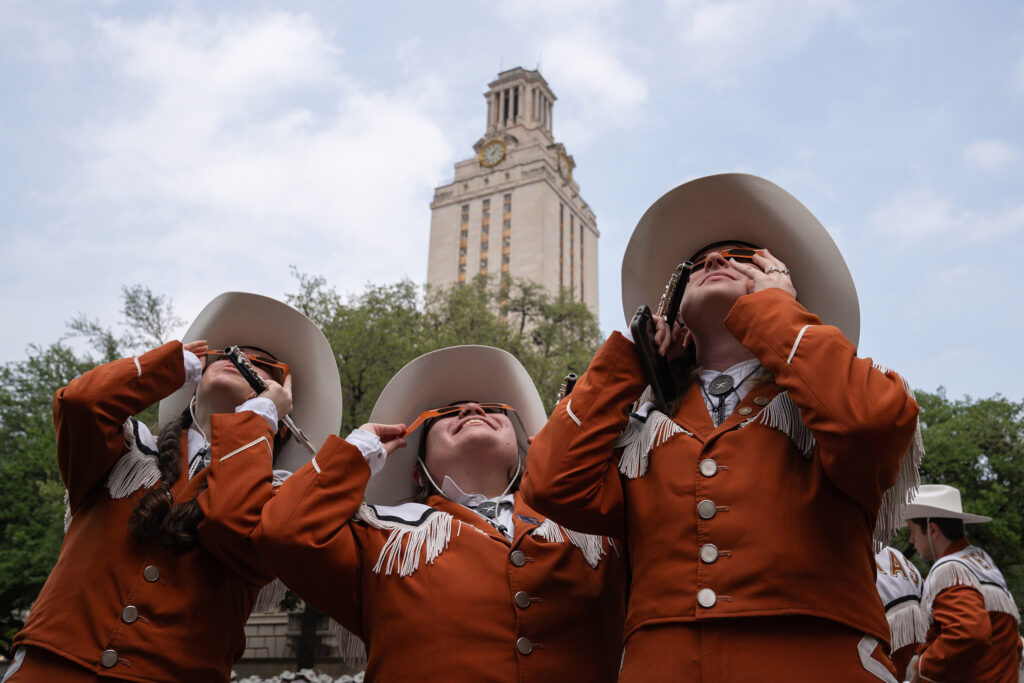UT Longhorn Band members looking up at the eclipse with the UT Tower in the background.